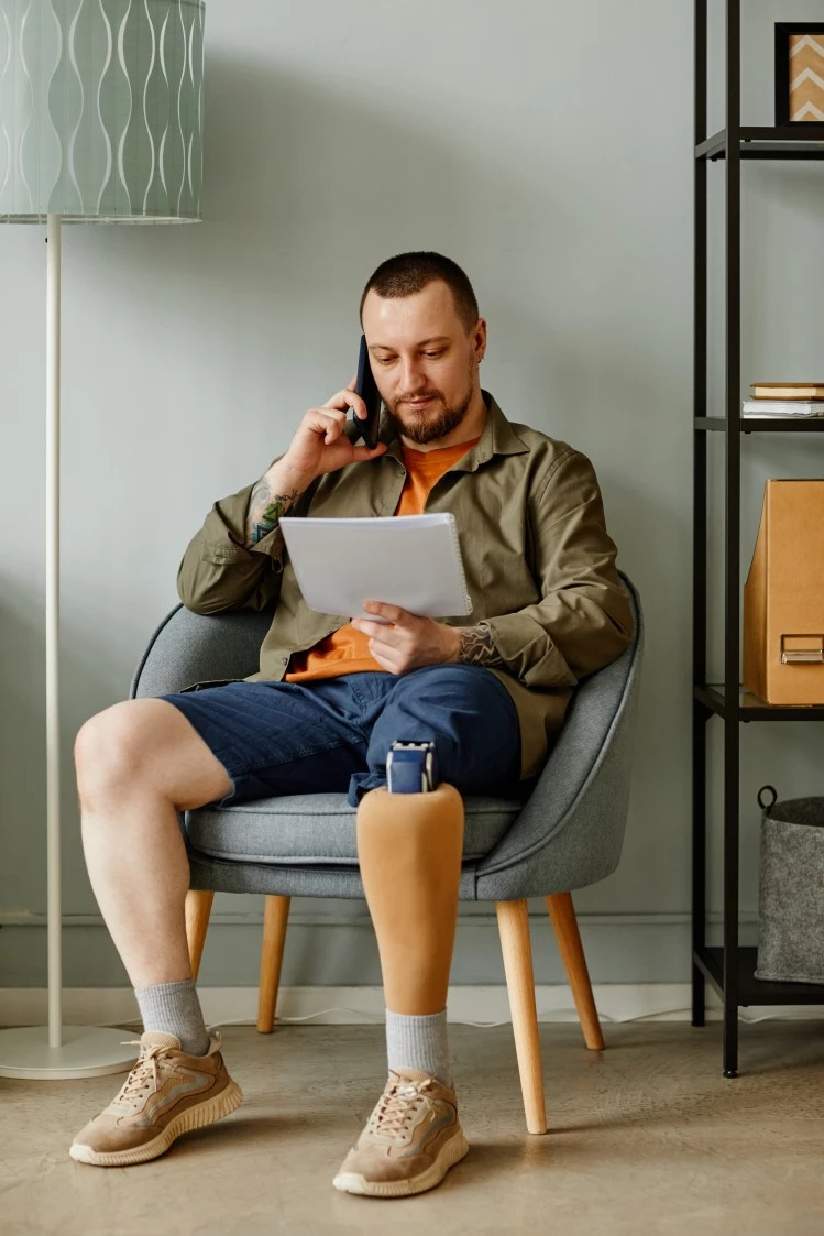 Disabled man with amputated leg sitting in chair making phone call