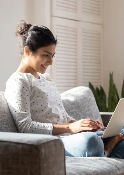 Happy woman sitting on couch with laptop making NDIS referral