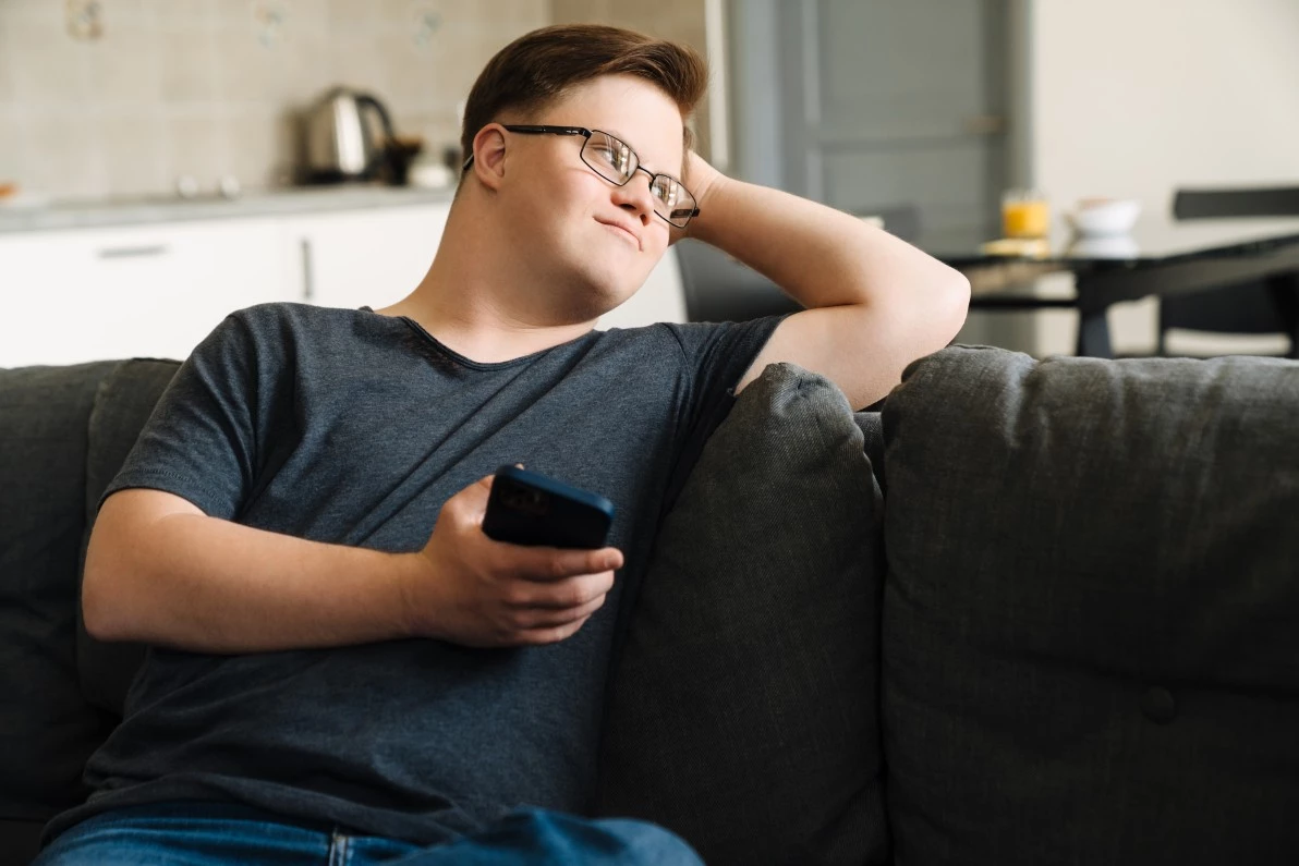 Disabled man with down syndrome sitting on couch holding mobile phone