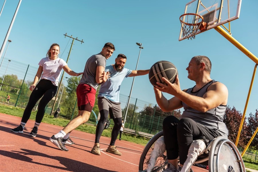 Disabled man in wheelchair playing basketball outside with friends