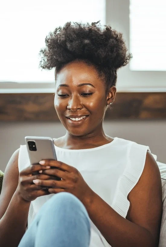 Happy woman sitting on couch using mobile phone to contact Fawn Assistive Care