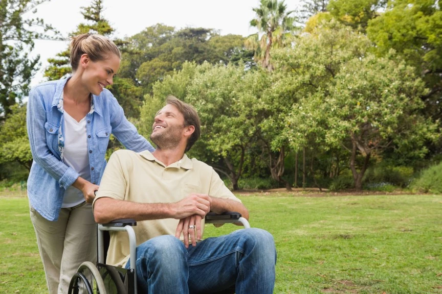Disabled man in wheelchair in park with carer looking up and smiling at carer
