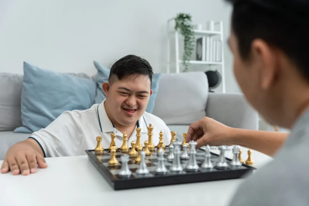 Disabled boy playing chess at home with carer