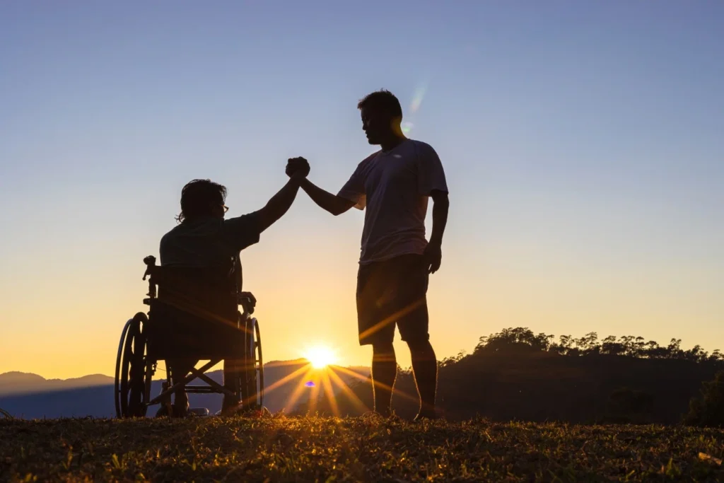 Two people, one person in wheelchair, standing outside holding hands at sunset